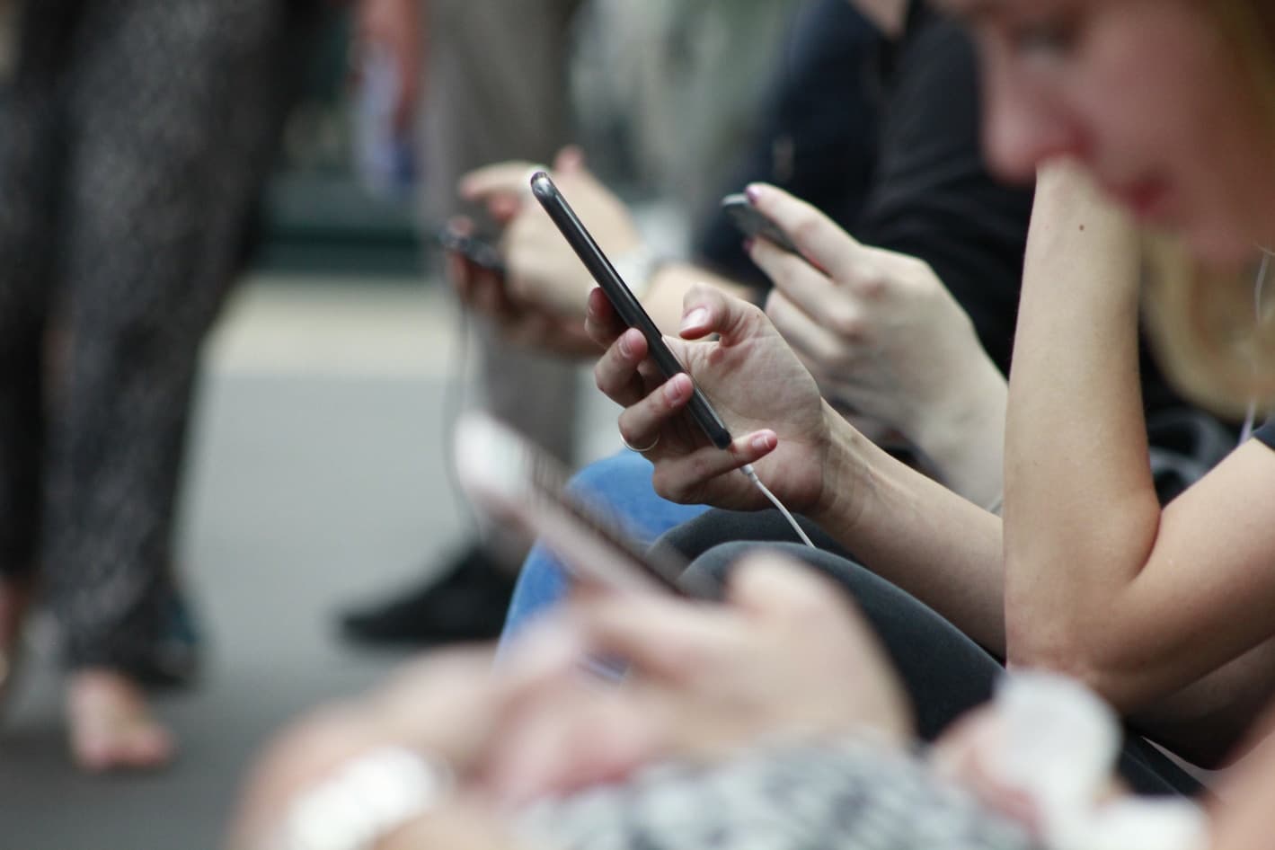 A row of people seated outdoors, each absorbed in a phone screen